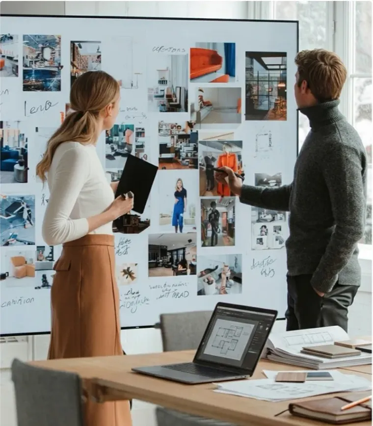 Two colleagues reviewing a mood board pinned across a studio wall